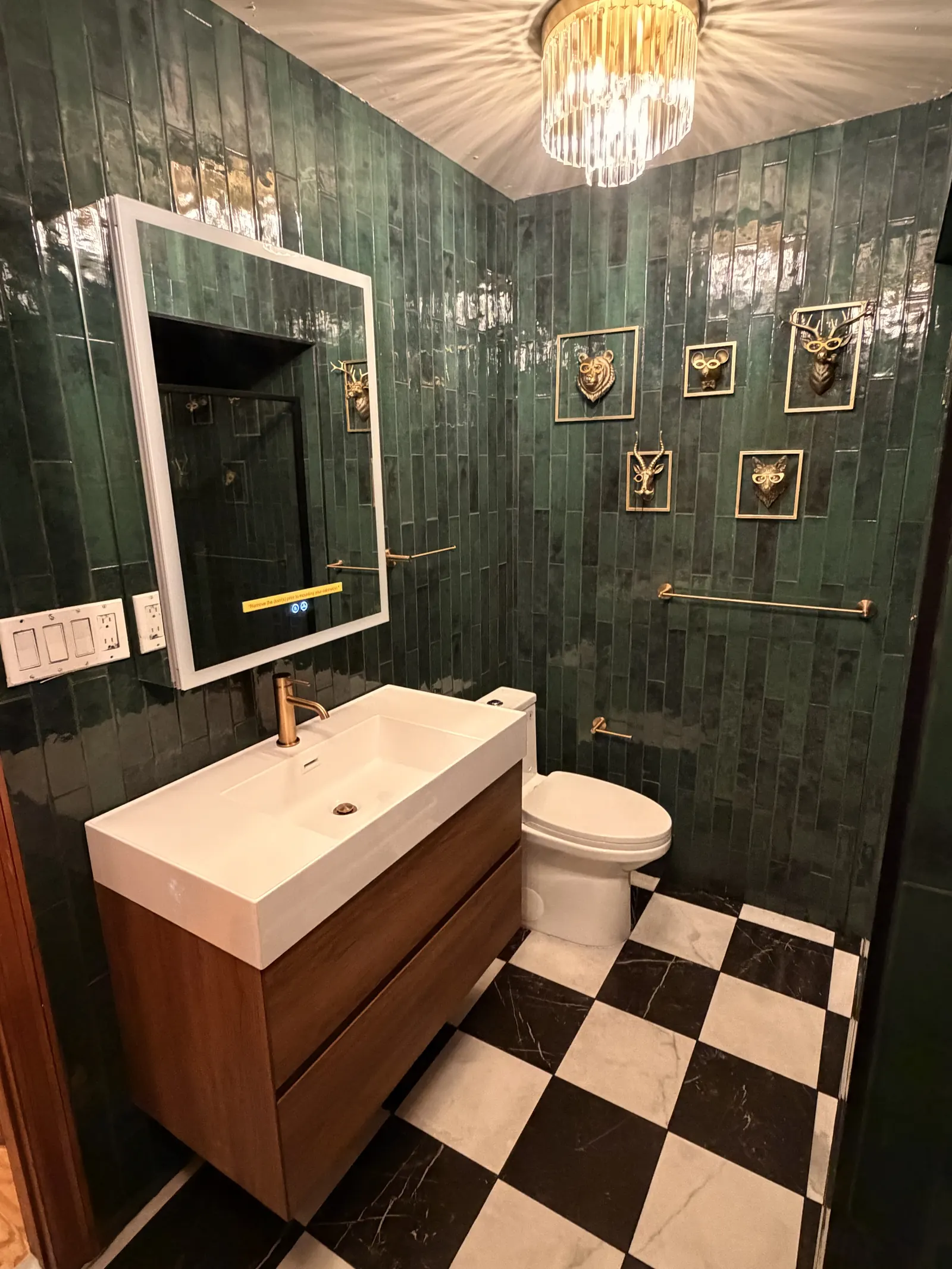 Powder room with green glazed vertical tile, floating walnut vanity and black-and-white marble-look floor